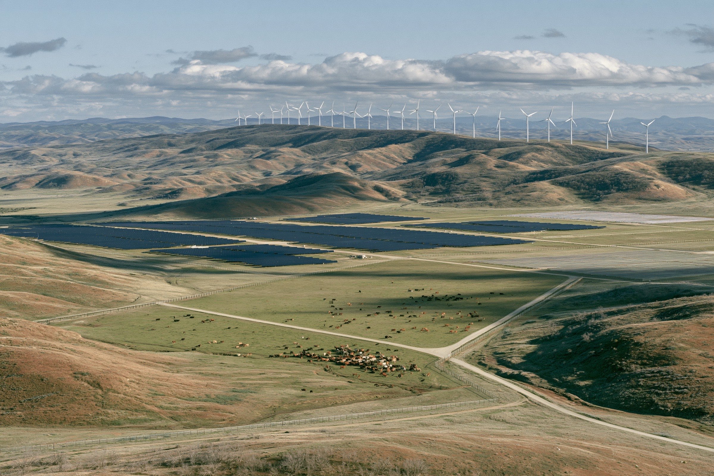 A working ranch valley with solar arrays and wind turbines on the ridge