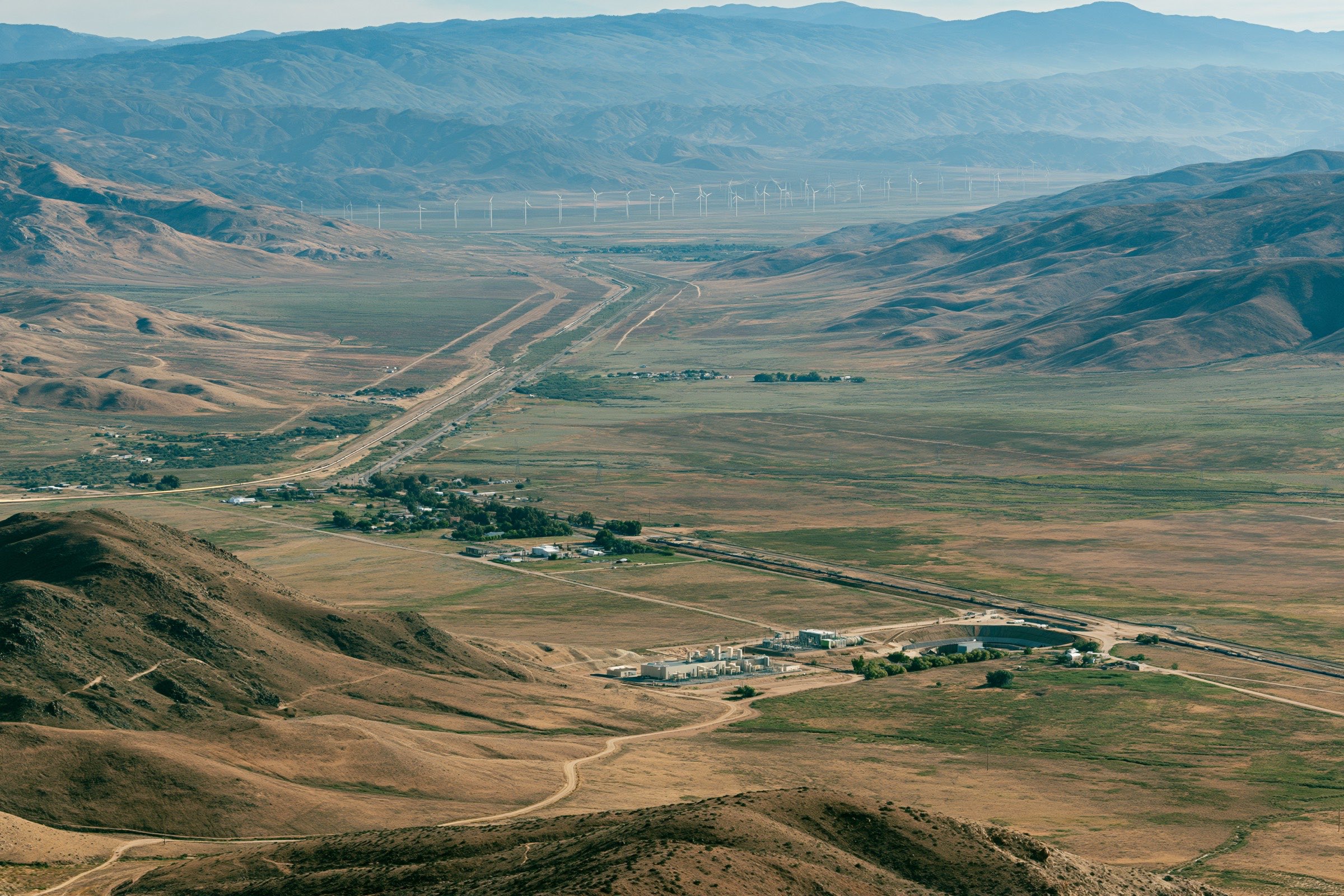 A desert valley with an infrastructure corridor running toward distant wind turbines